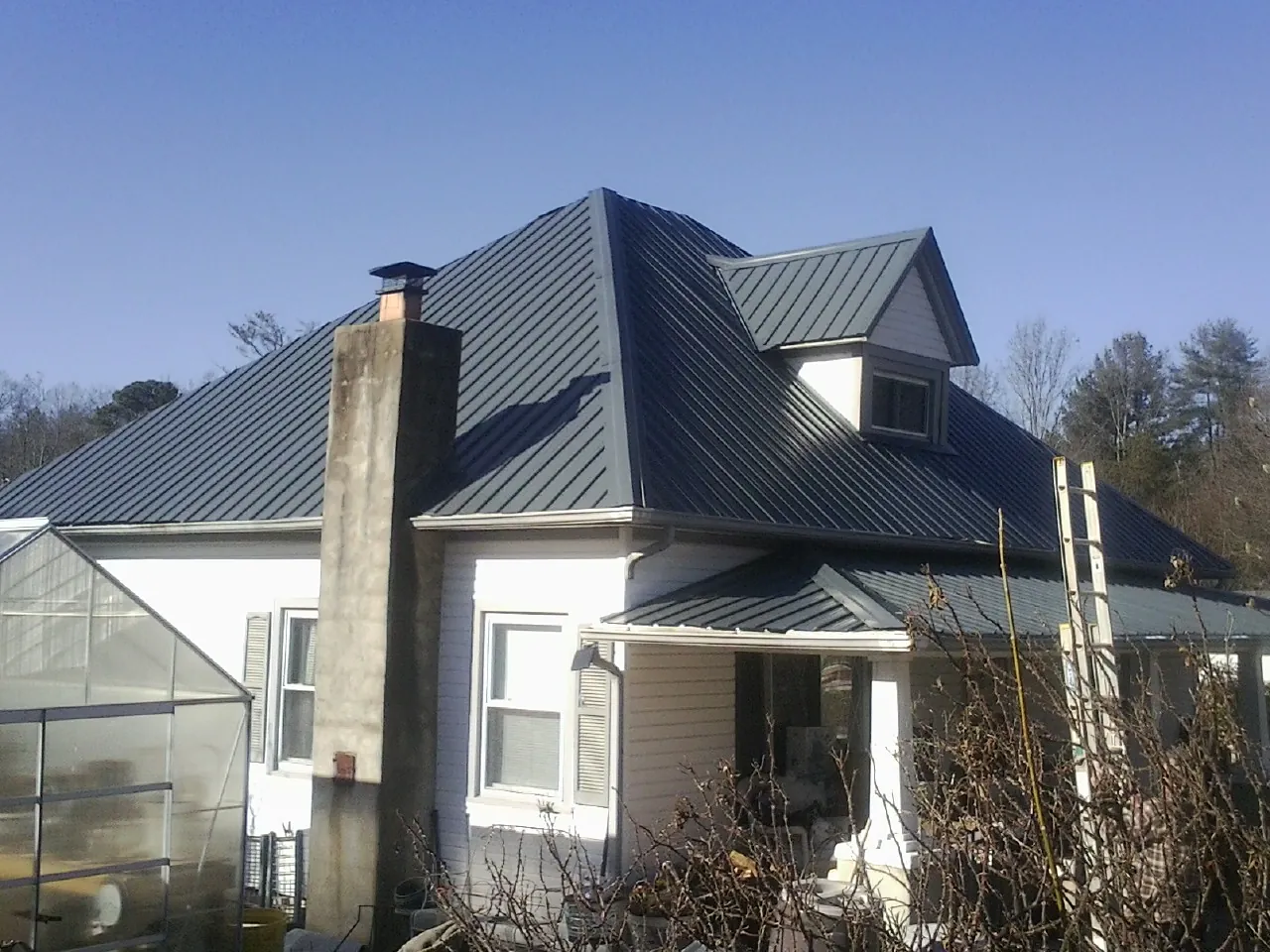 Dark blue standing seam metal roof on a white farmhouse with dormer — Slate & Tile Roof Repair by Roofing Brothers in Moyie Springs