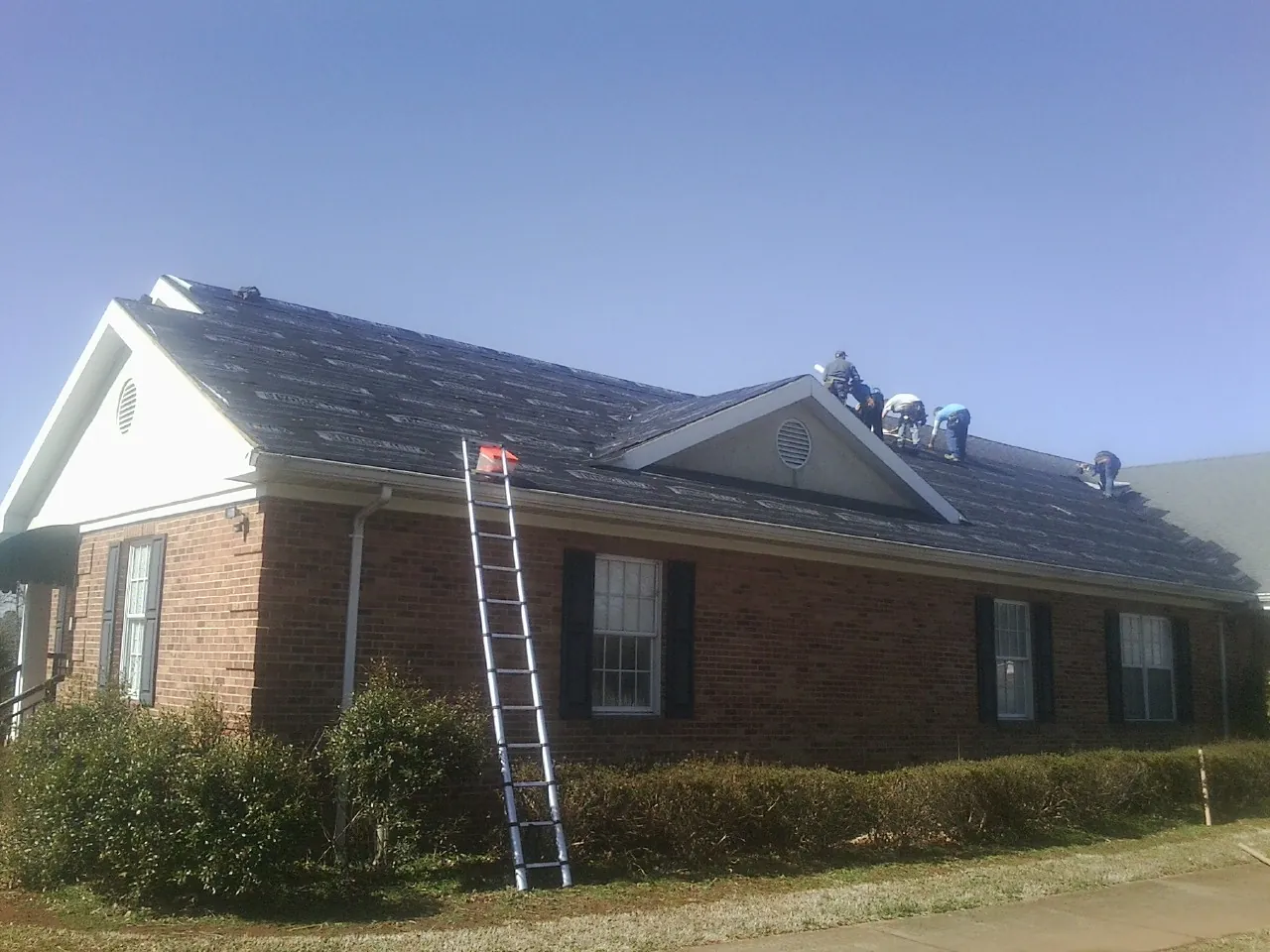 Crew tearing shingles off a brick ranch roof with a ladder set — Metal Roof Repair work by our crew in Moyie Springs