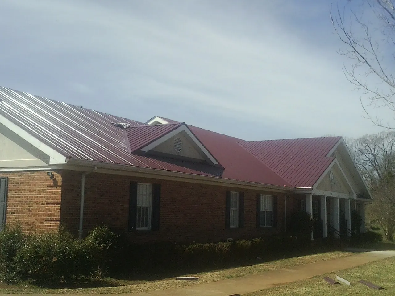 Red metal roof with gabled entries on a long brick building, from a Hail Damage Roof Repair job in Moyie Springs