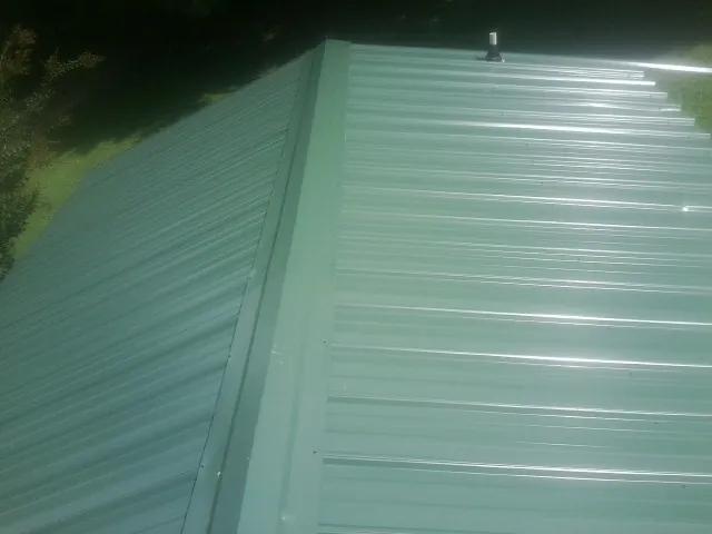 New green metal panels meeting at the ridge of a roof — Flat Roof Repair work by our crew in Moyie Springs