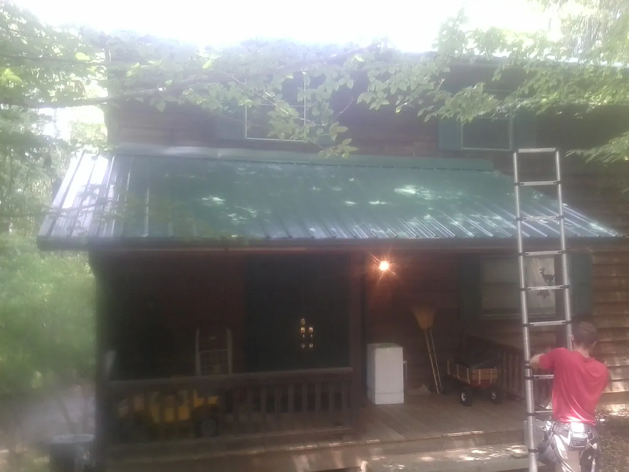 Worker on a ladder at the green porch roof of a wooded cabin in Moyie Springs