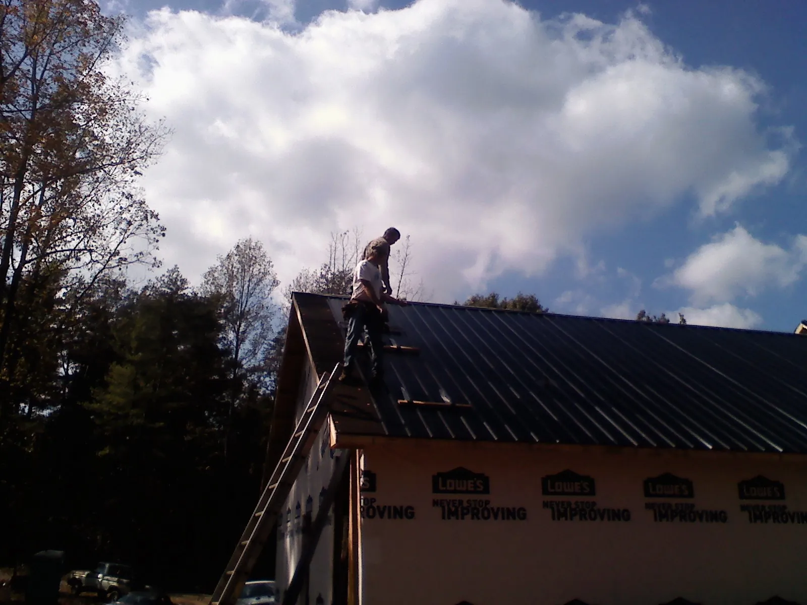 Roofer fastening dark metal panels high against a cloudy sky, from a Roof Inspection job in Moyie Springs
