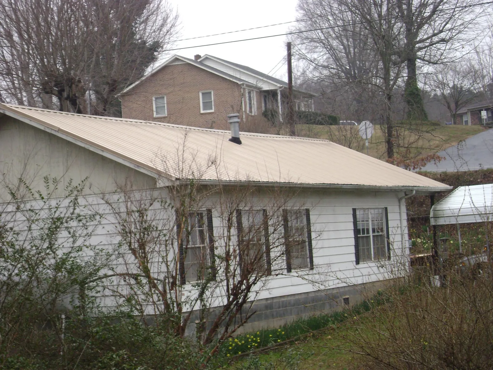 Tan metal roof on a white sided house set into a hillside — Commercial Roofing by Roofing Brothers in Moyie Springs